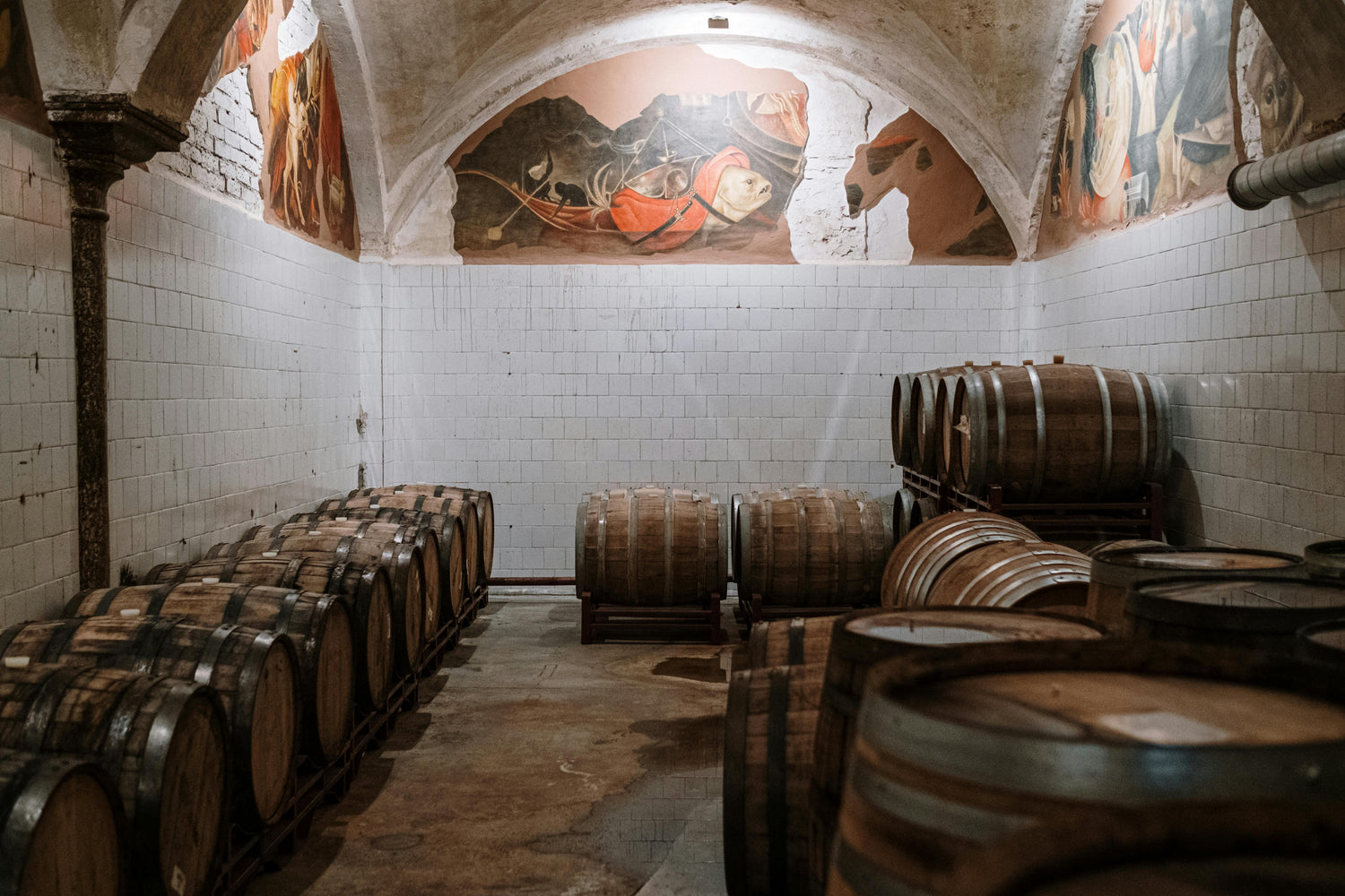 Old wine barrels in cave with artworks on vaulted ceiling